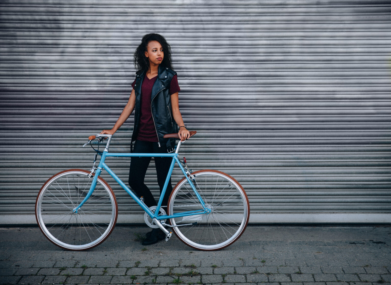 African American teenage girl standing on a city street with her fixed gear bicycle in front of urban graffitti